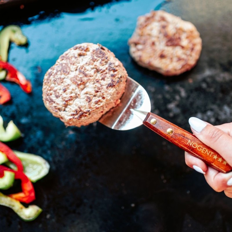 pelle de cuisine en bois de merisier de 9 cm utilisée pour retourner un burger sur une plancha avec légumes.