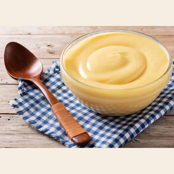 Crème pâtissière lisse dans un bol en verre avec cuillère en bois sur nappe à carreaux