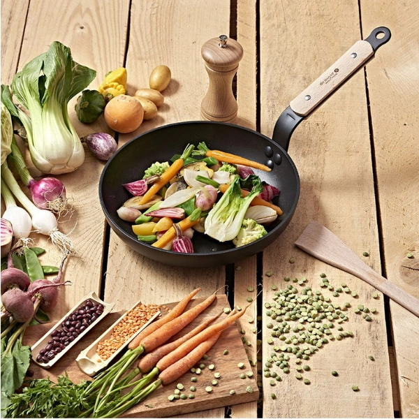 Wok antiadhésif De Buyer avec légumes frais colorés sur plan de travail en bois