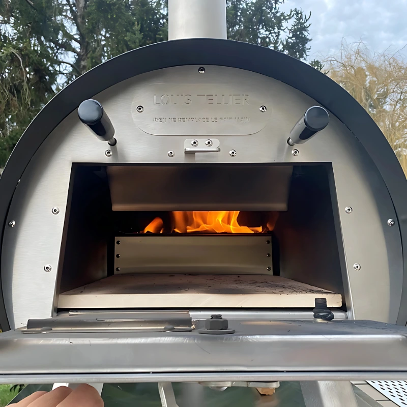 Four à bois extérieur Marcel de Louis Tellier en inox allumé, avec flammes visibles à l'intérieur
