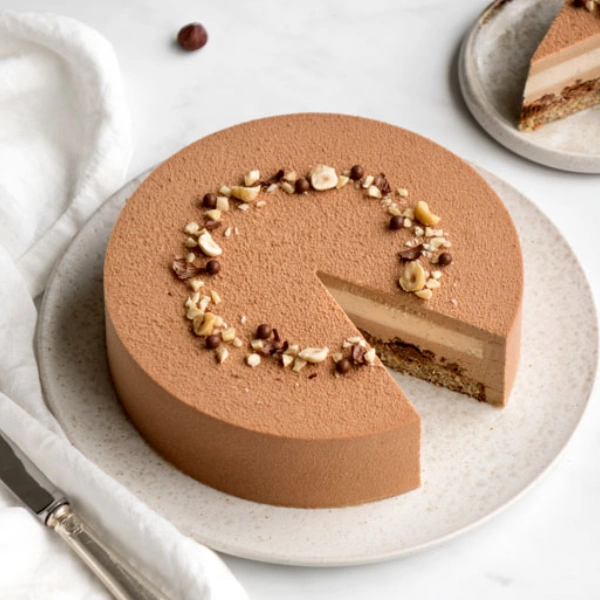 Entremets chocolat noisette avec insert praliné et décor croquant, présenté sur assiette en marbre