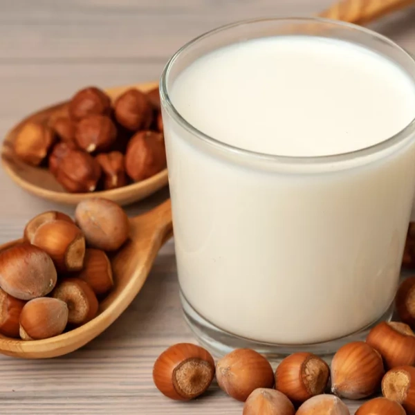 Verre de lait de noisette avec noisettes entières sur cuillères en bois, posé sur fond en bois clair