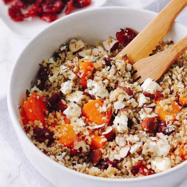 Salade de boulgour aux abricots secs, feta, noisettes concassées et canneberges, servie dans un bol blanc