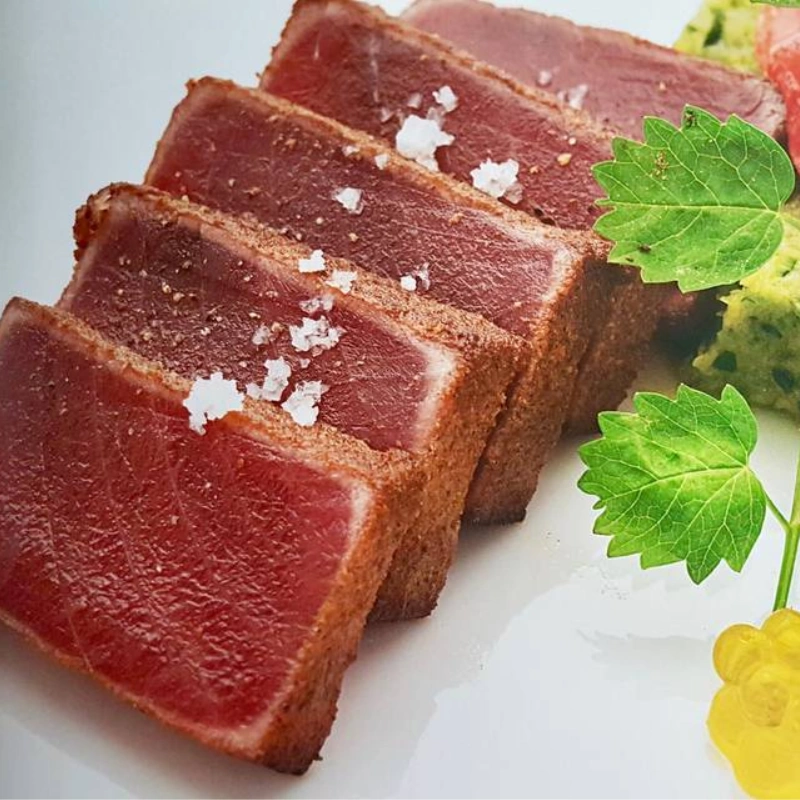 Tranches de thon mi-cuit avec croûte d'épices et gros sel, servies avec une garniture verte