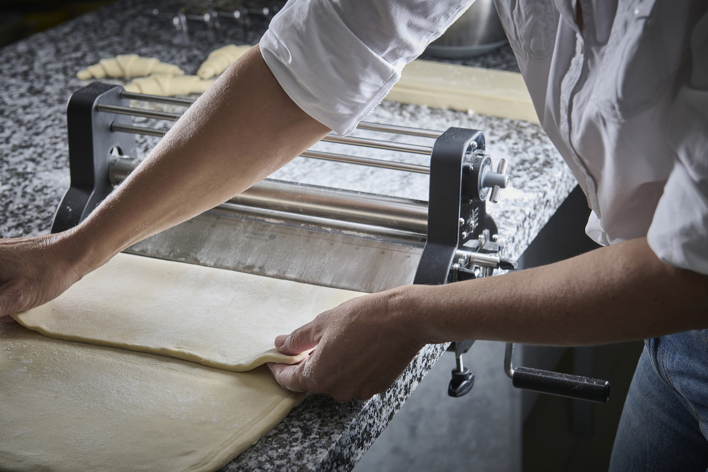 Laminoir à pâte utilisé pour étaler une pâte, avec une main ajustant la position de la pâte sur la machine.