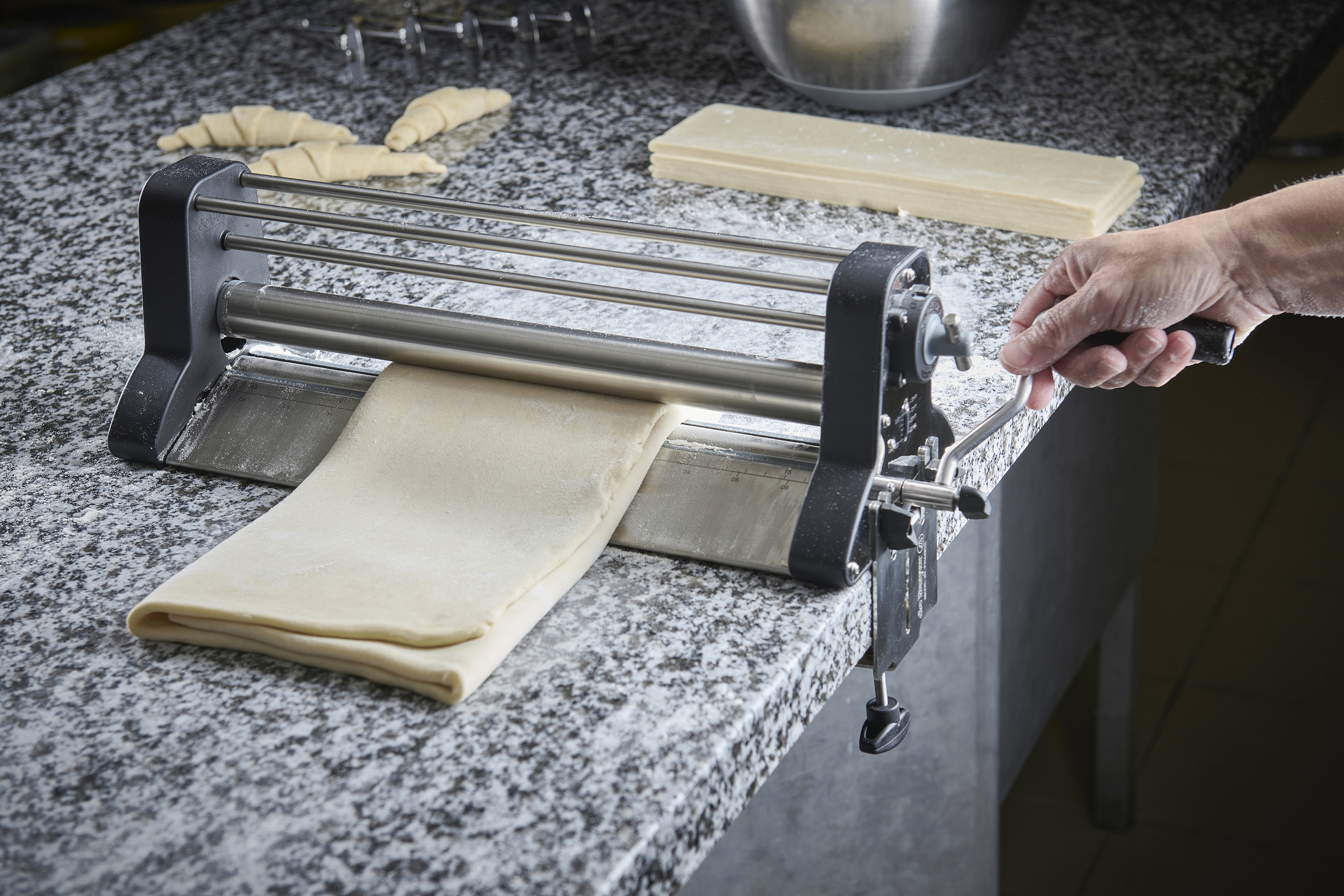 Pâte feuilletée fraîchement laminée à l’aide d’un laminoir, avec des croissants en préparation en arrière-plan