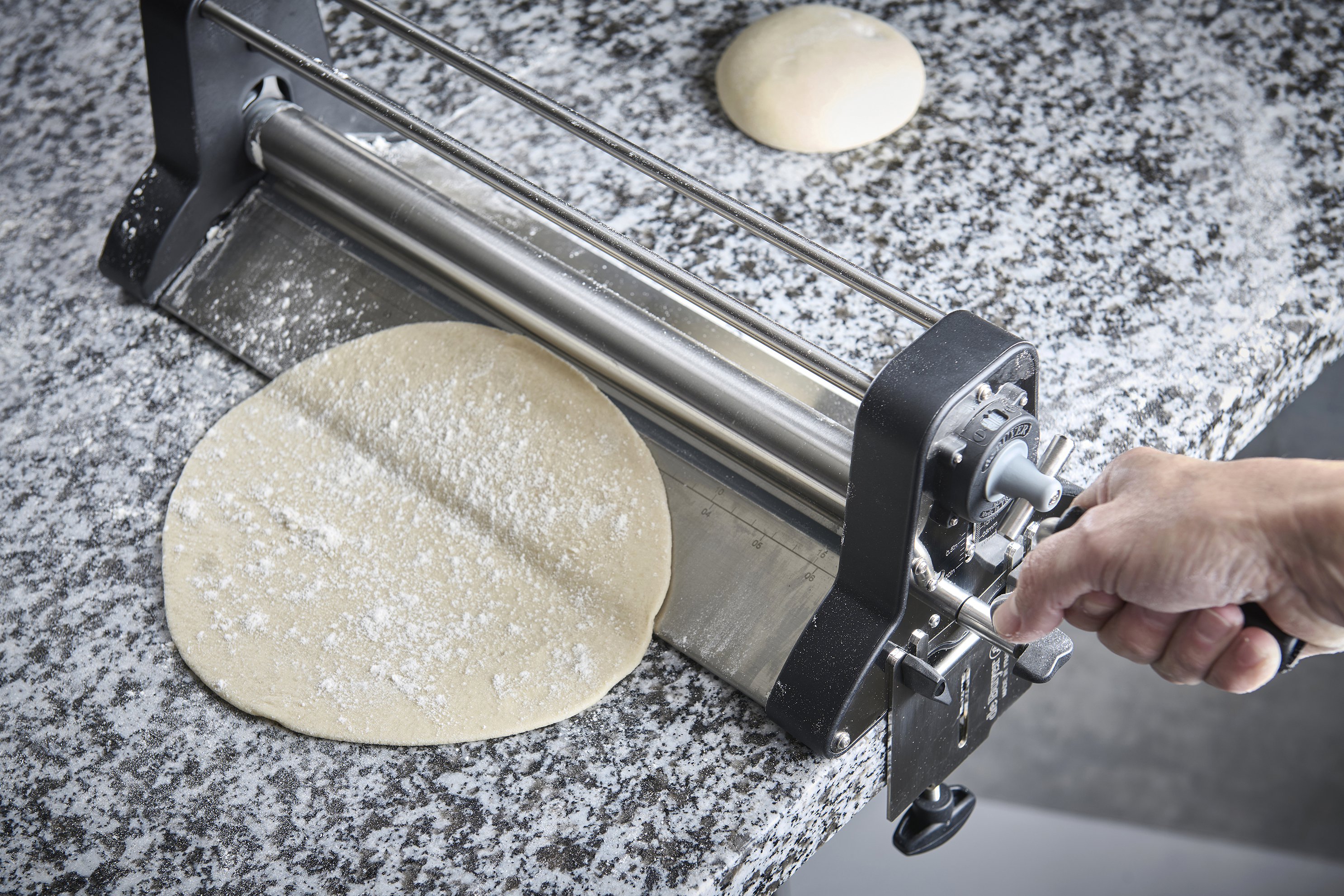 Laminoir à pâte en action avec une pâte à pizza aplatie sur un plan fariné.