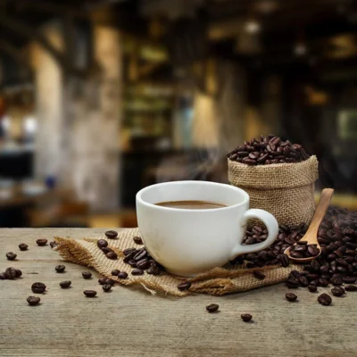 Tasse de café fumant posée sur une toile de jute avec grains de café et cuillère en bois – ambiance chaleureuse du matin